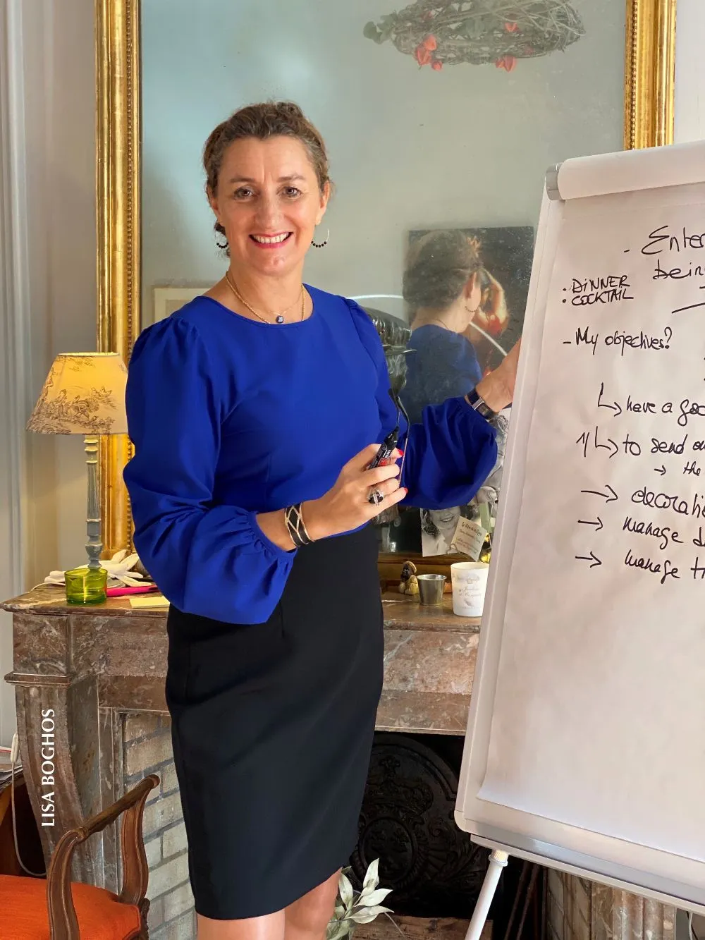 France de Heere animant un atelier de savoir-vivre et d'aisance sociale à Versailles, expliquant les codes de l'élégance sur un tableau blanc.