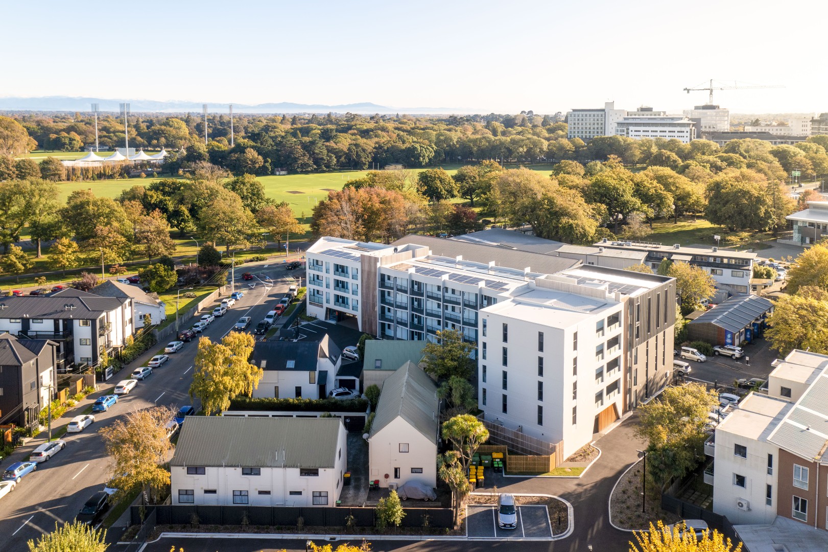 Aerial view of urban buildings near a large green park with trees and sports fields in daylight.
