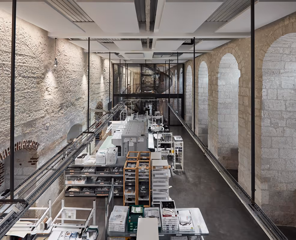 Intérieur d'une imprimerie moderne avec murs en pierre et grandes arches, contenant plusieurs machines d'impression et tables de travail organisées.