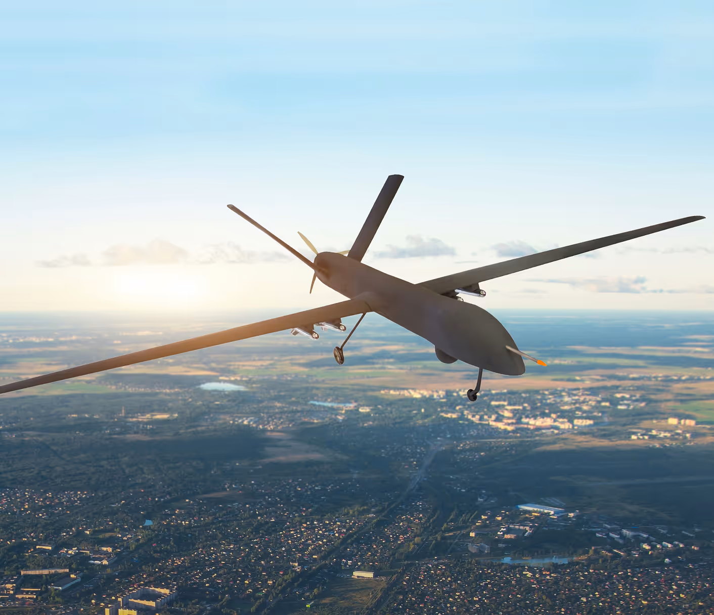 Drone militaire muni de missiles volant au-dessus d'une ville au coucher du soleil.