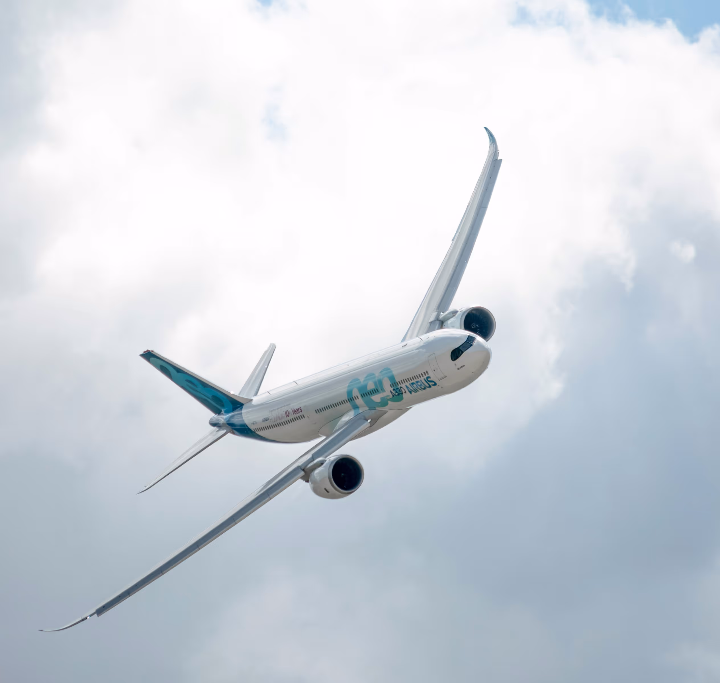 Avion Airbus A350 en vol, vu de dessous avec un ciel nuageux en arrière-plan.