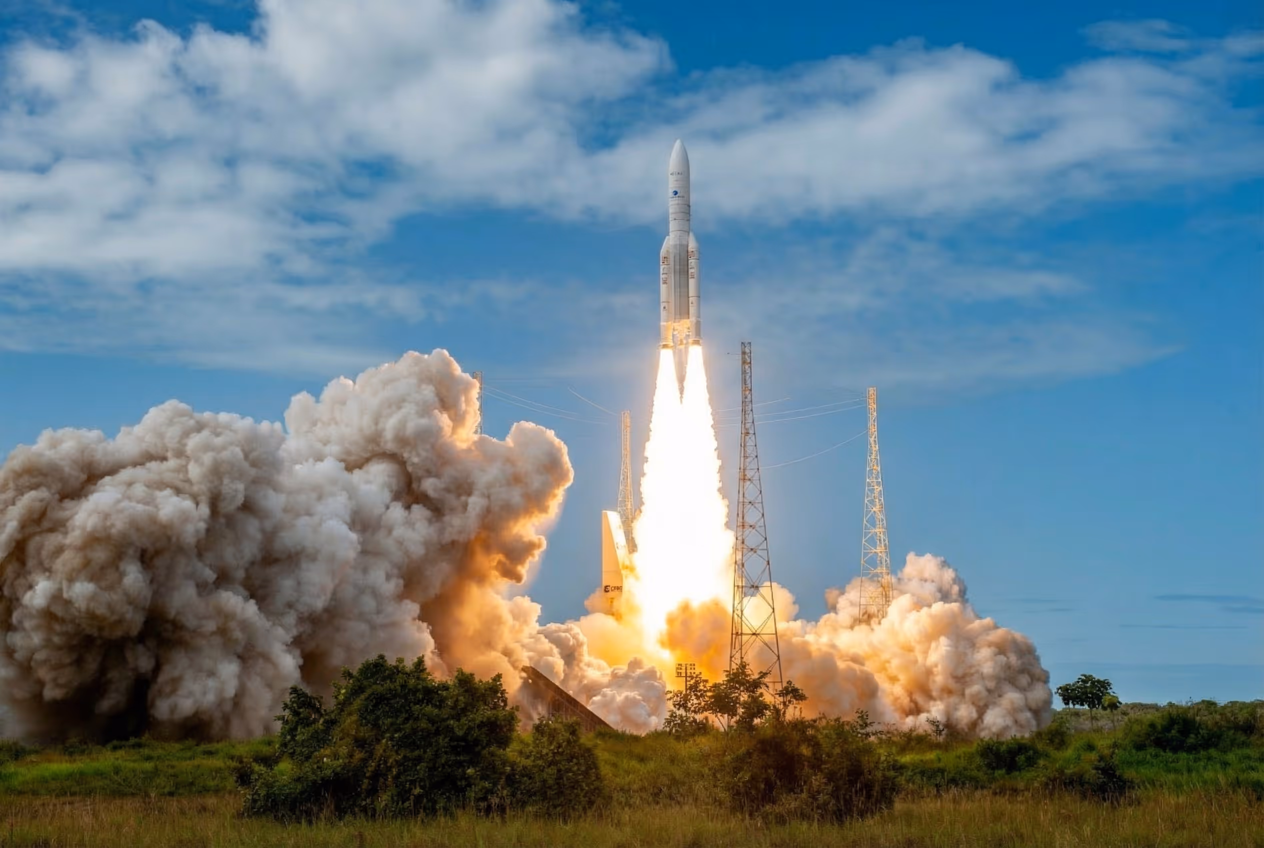 Lancement d'une fusée avec un épais nuage de fumée à la base sous un ciel bleu partiellement nuageux.