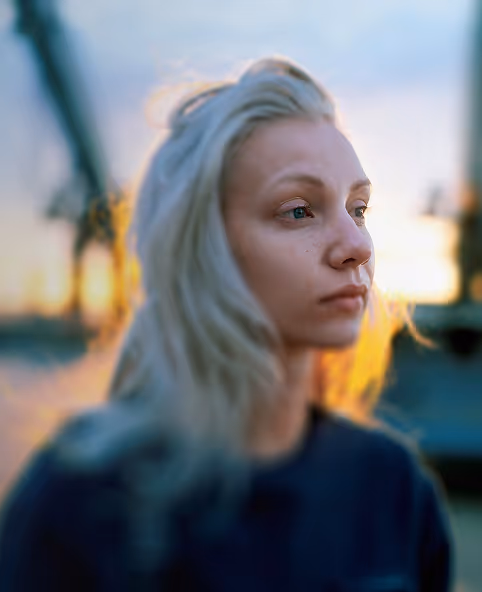 Young woman with long blonde hair looking thoughtfully to the right with a sunset background.