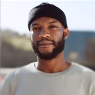 Close-up of a man with a beard wearing a black beanie and light-colored shirt outdoors.