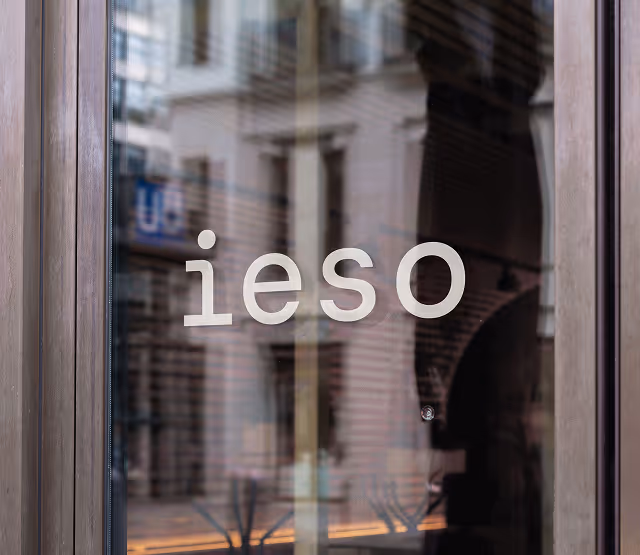 Glass door with the word 'ieso' in white lowercase letters and a blurred reflection of buildings behind.