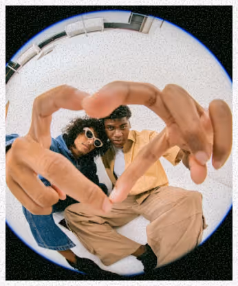 Deux jeunes personnes assises au sol formant un cœur avec leurs mains devant un objectif fisheye.