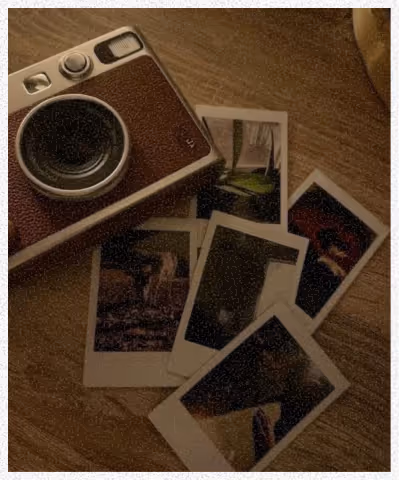 Appareil photo argentique posé à côté de plusieurs photos instantanées éparpillées sur une table en bois.