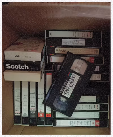 Boîte contenant plusieurs cassettes VHS et une cassette VHS noire posée en diagonale dessus.