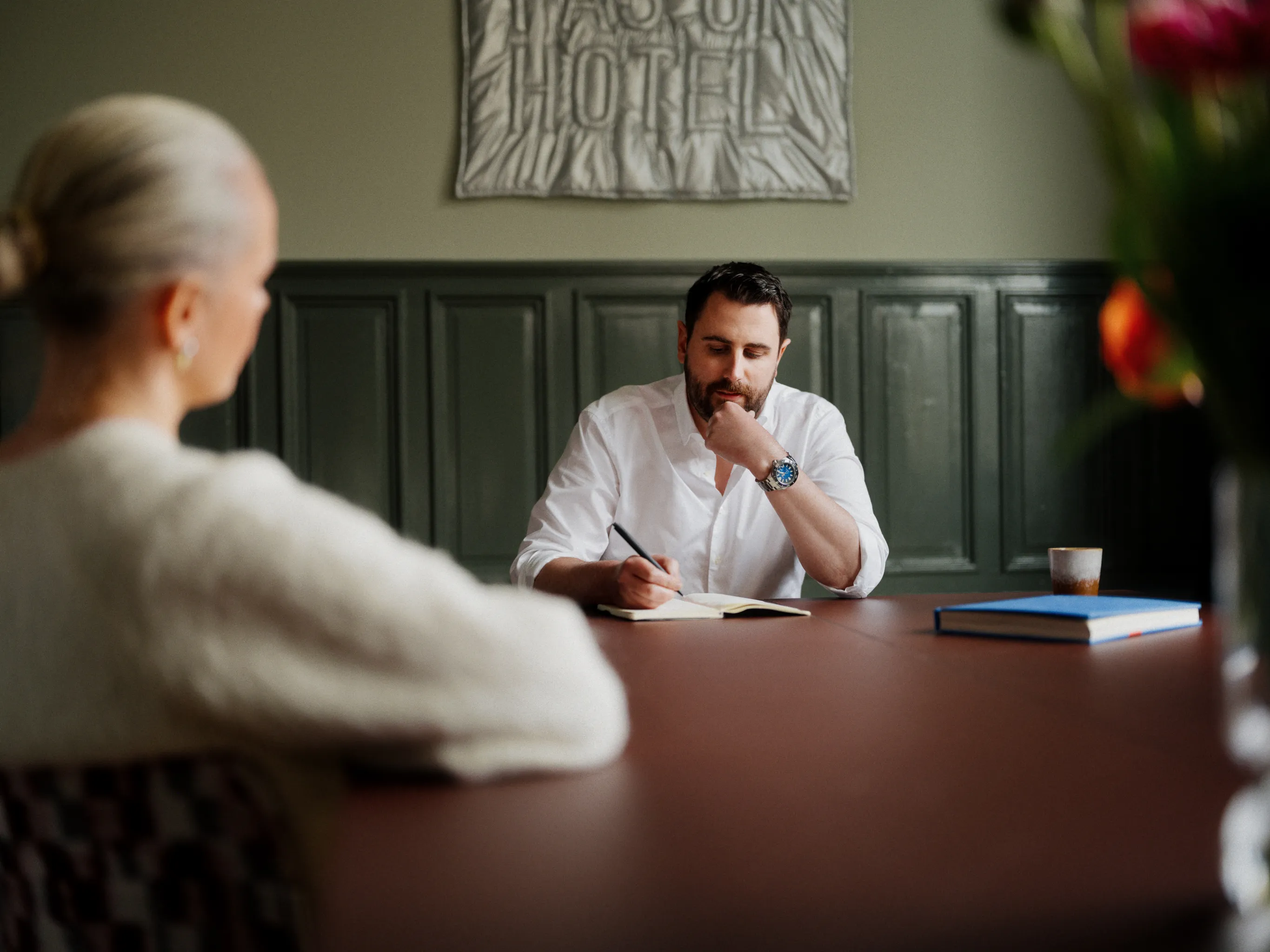 Man in a white shirt thoughtfully taking notes during a meeting.