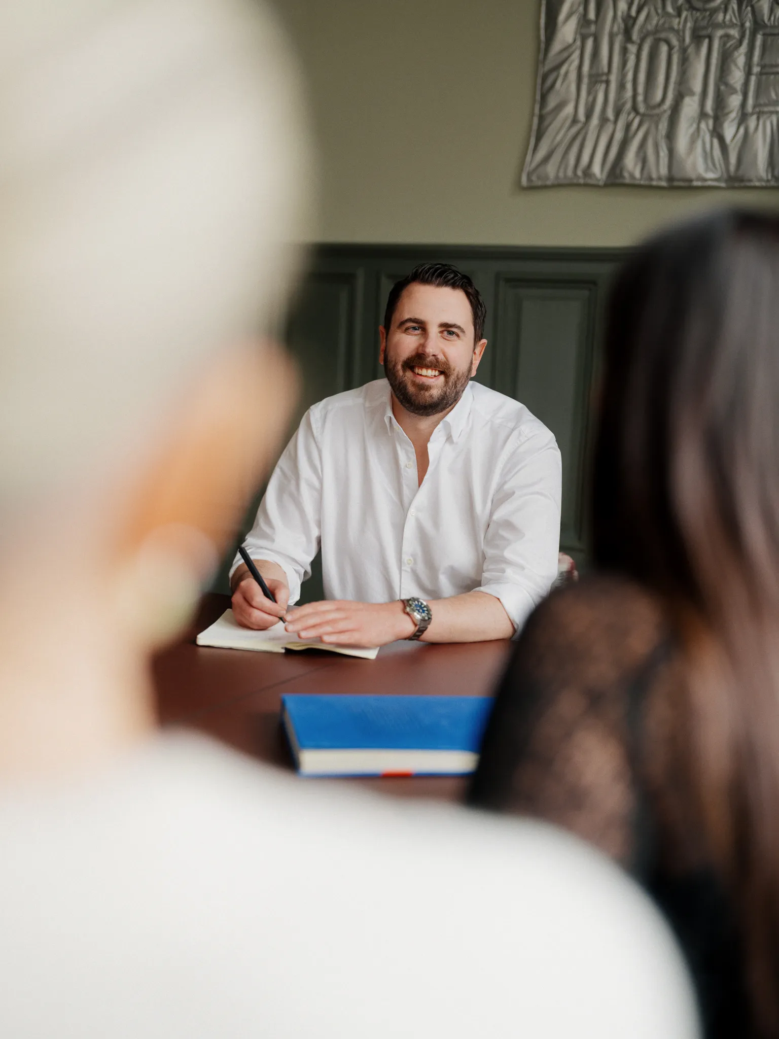 Consultant writing in a notebook during a collaborative meeting.