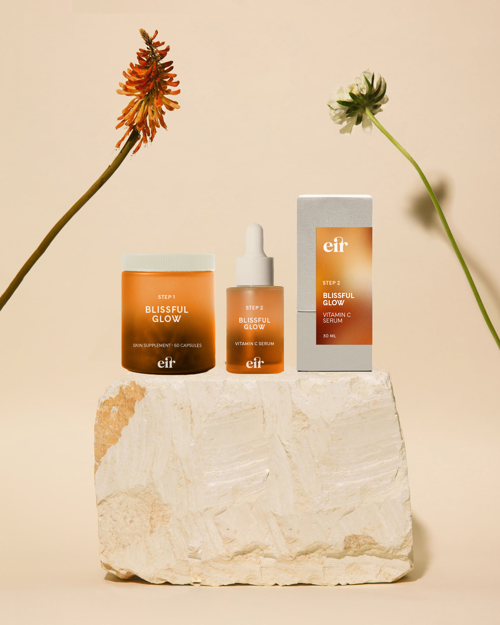 Cosmetics product packaging displayed on a stone with two flowers.