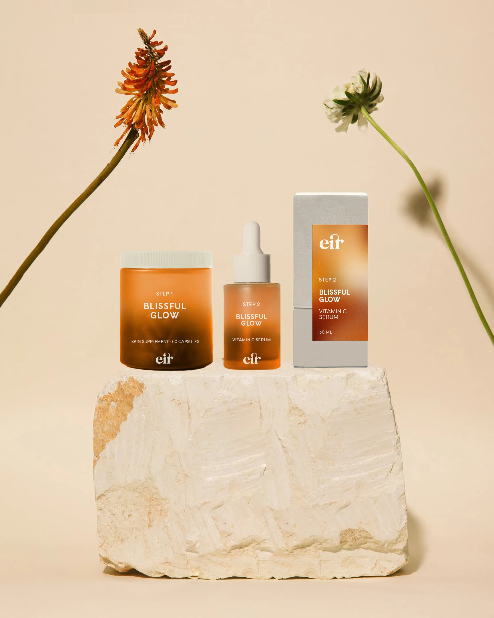 Cosmetics product packaging displayed on a stone with two flowers.