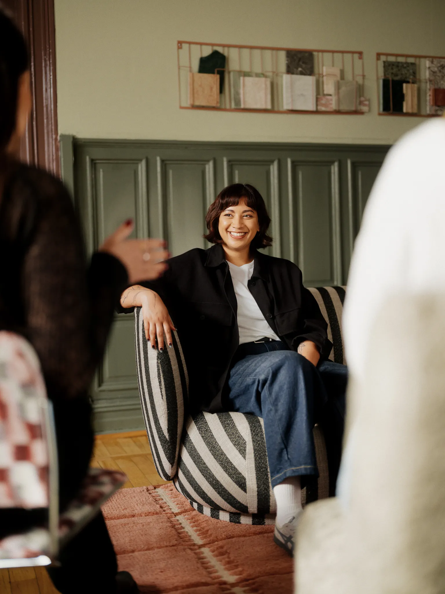 Consultant smiling on a striped sofa in a green wood-paneled room.