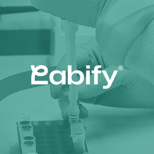 Gloved hand using a pipette to transfer liquid into a small vial in a laboratory setting with test tubes nearby, overlaid with the Labify logo.
