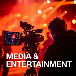 Cameraman filming a live event with red stage lights and blurred crowd in the background.
