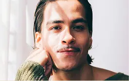Portrait of a young man with long dark hair resting his face on his hand with natural light shadows.