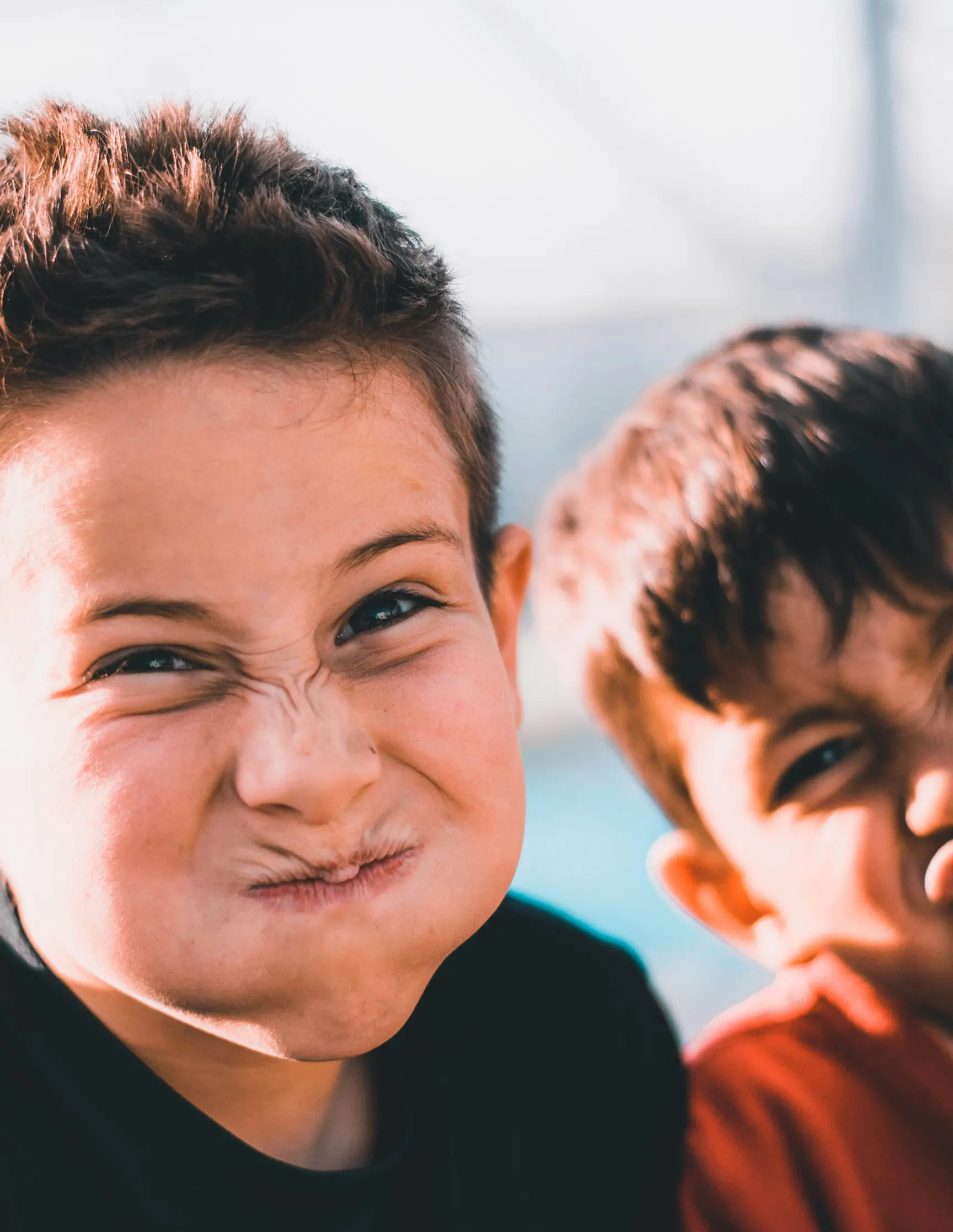 Two boys making funny scrunched faces, one puffing cheeks tightly.