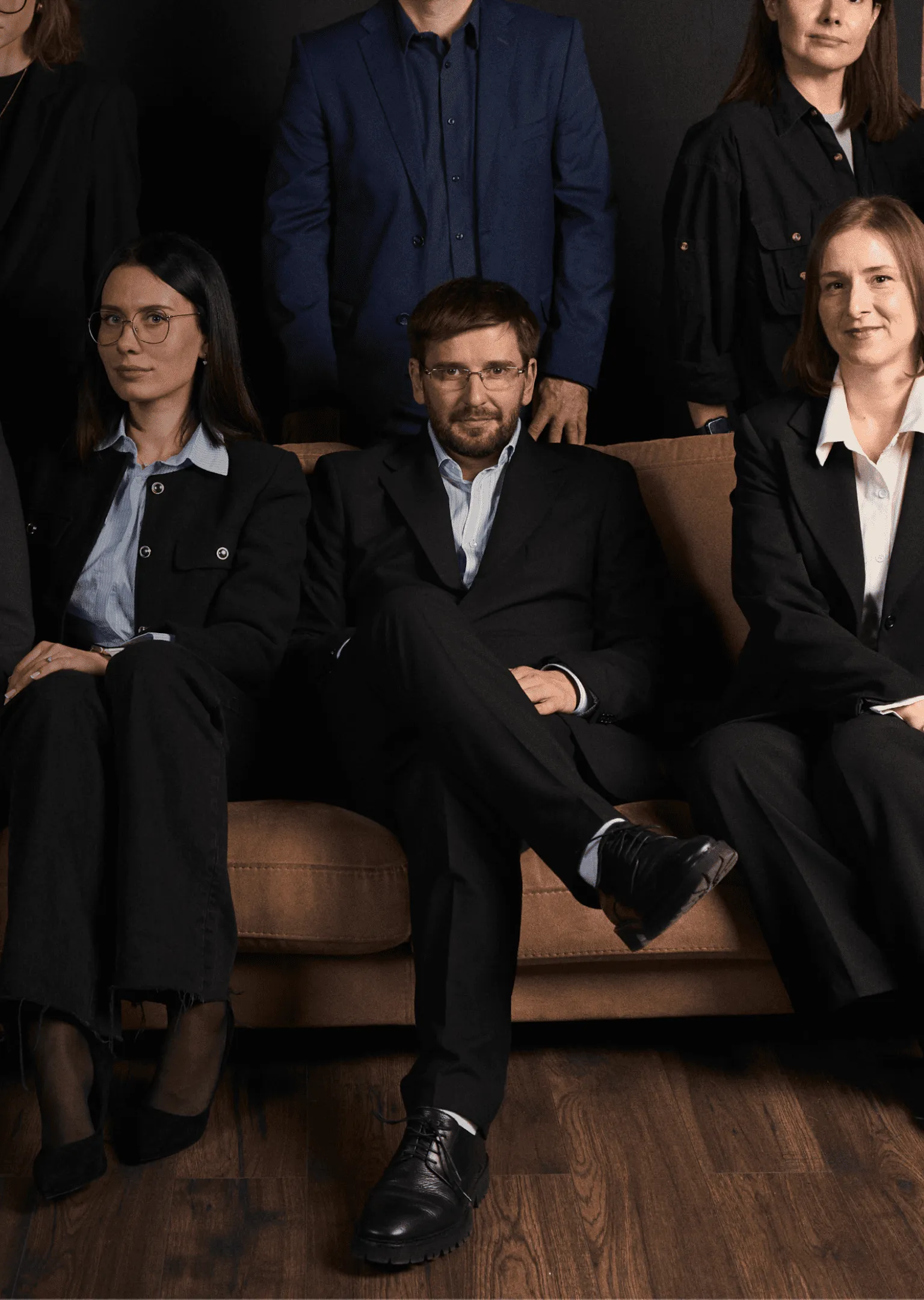 Group of professionally dressed men and women sitting and standing against a dark background with wooden floor.
