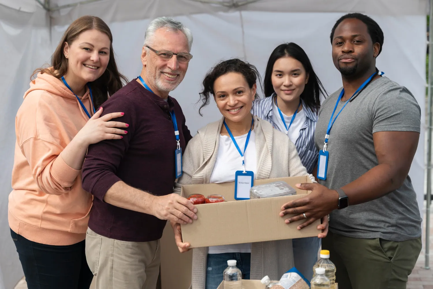 Group of five diverse volunteers smiling and holding a cardboard box with food donations.