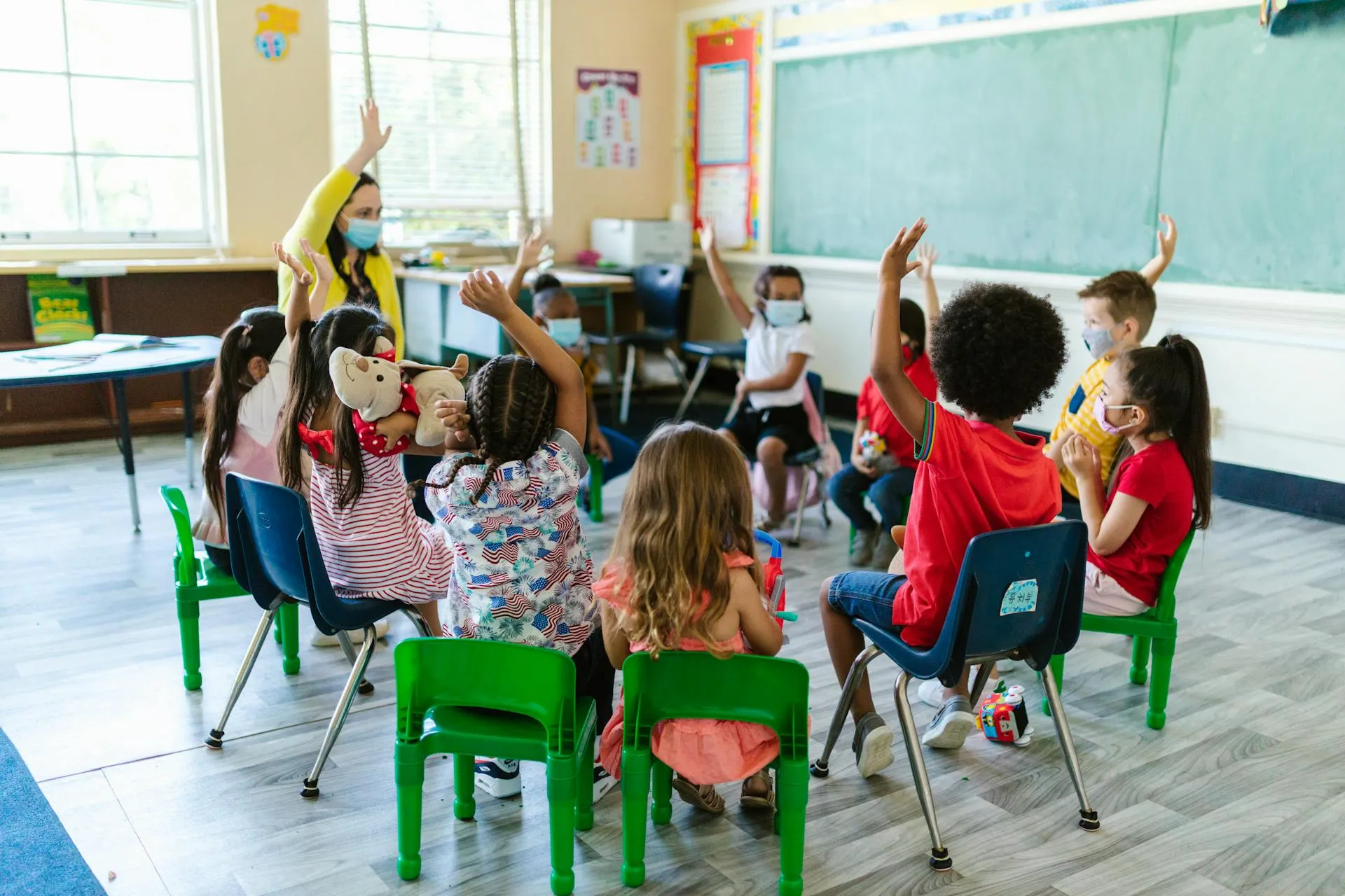 Young child drawing with markers at a classroom table with other children in the background.