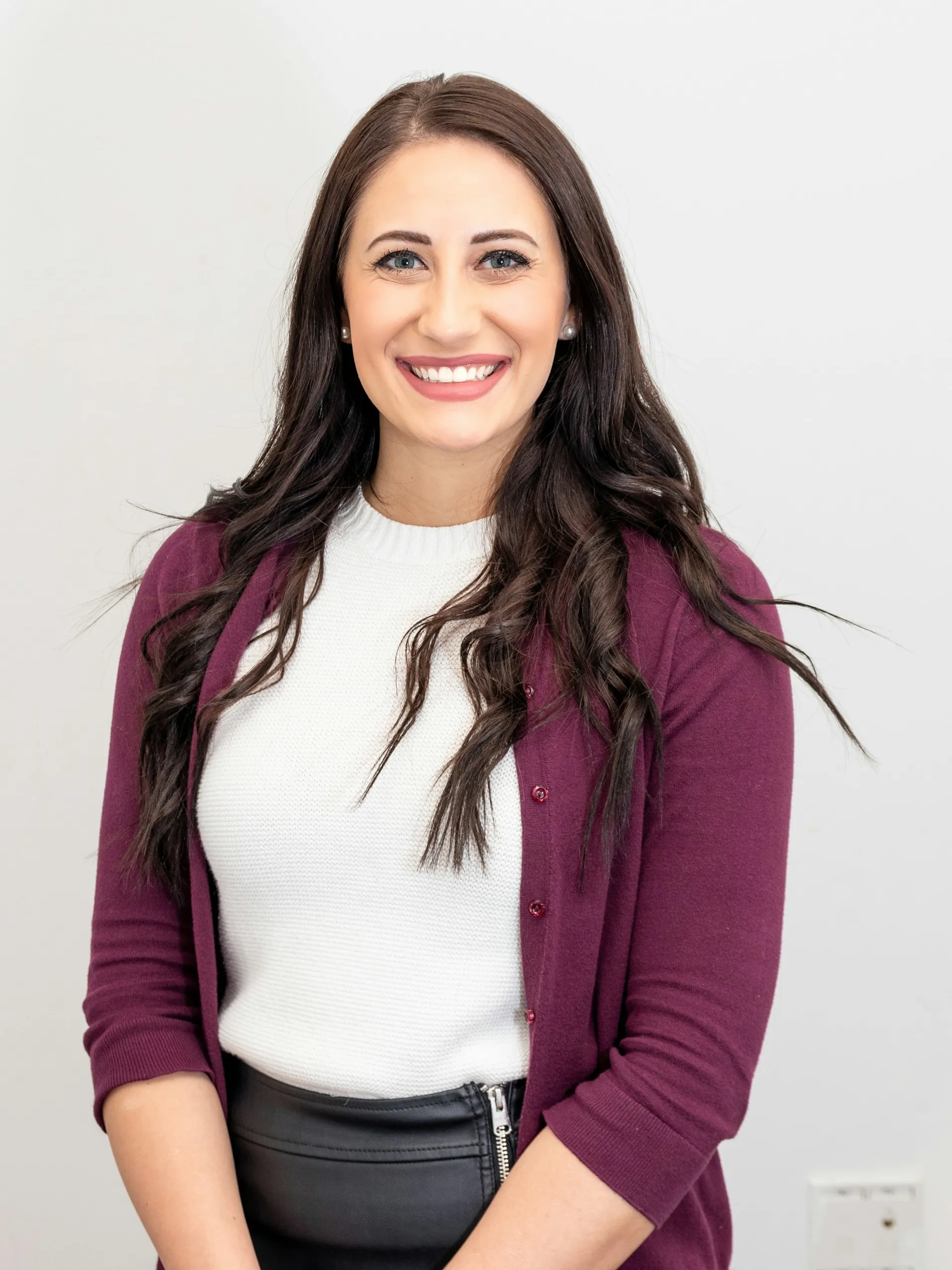 Smiling woman with long dark hair wearing a white sweater and purple cardigan.