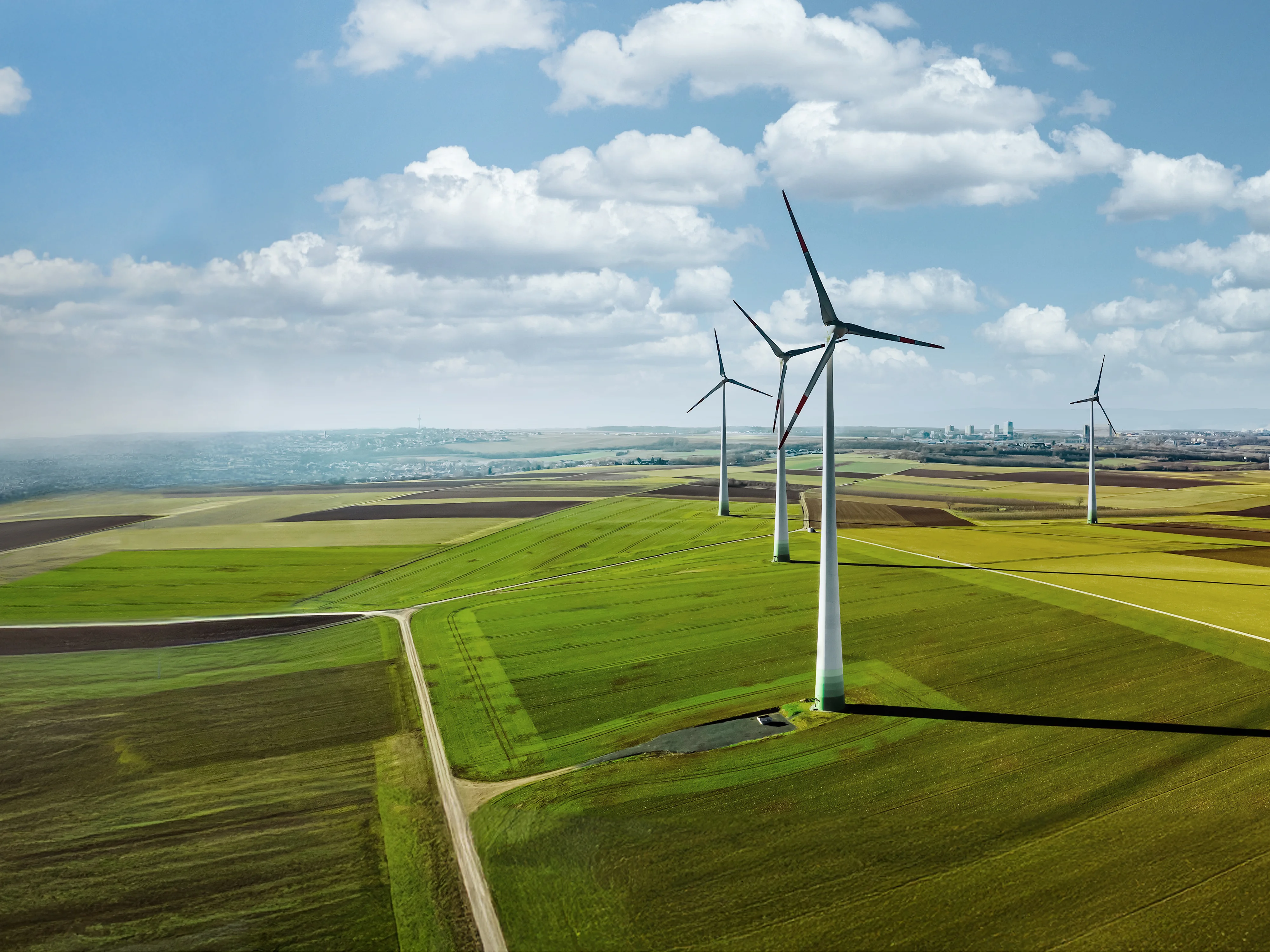 Landschaft mit grünen Feldern und mehreren Windkraftanlagen unter blauem Himmel mit Wolken.