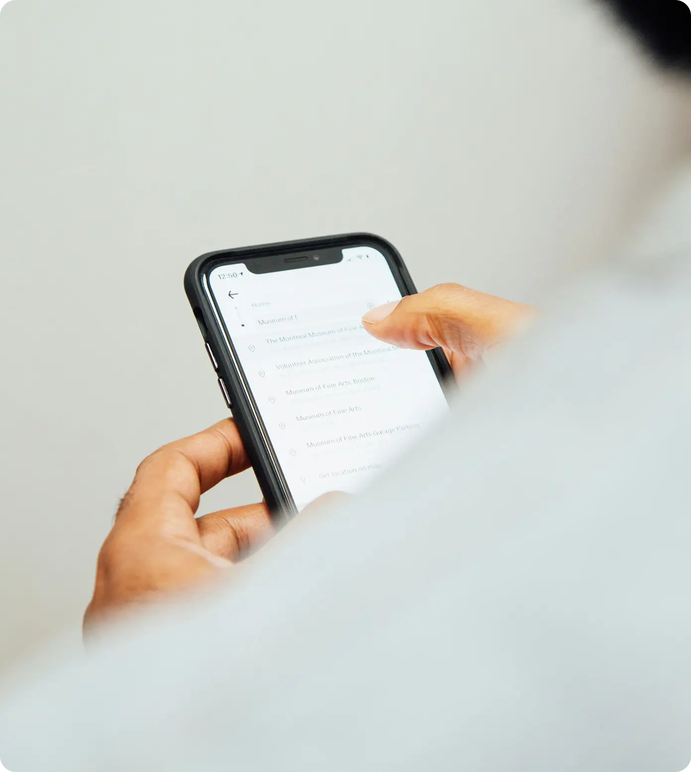 Person holding a smartphone displaying a list of museums on a white interface.
