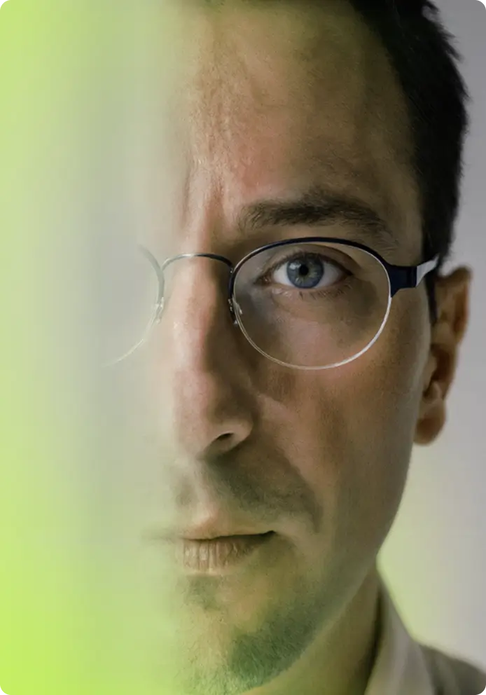 Close-up portrait of a man wearing round glasses with a greenish light effect partially obscuring the left side of his face.