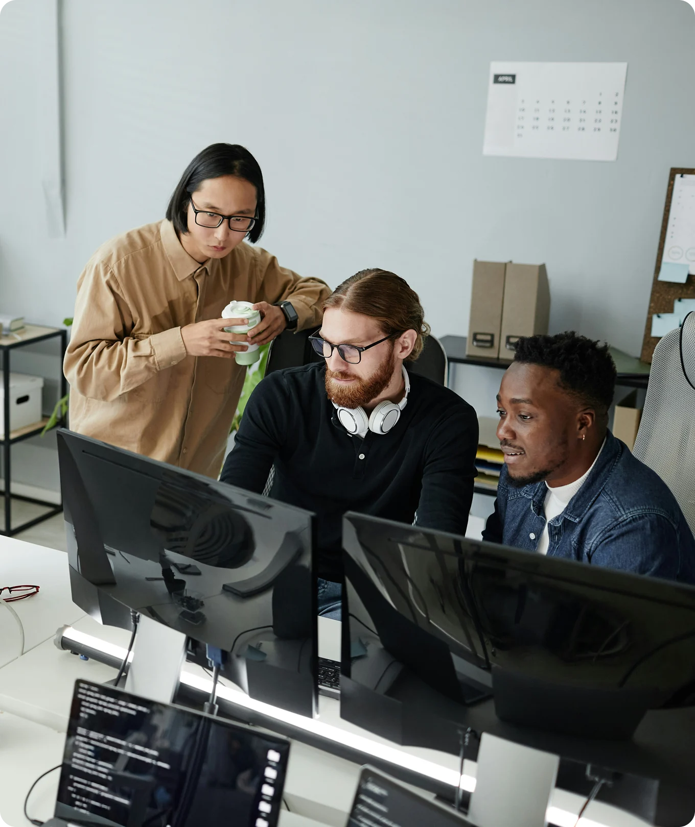 Three men collaborating and looking at computer screens in an office workspace.