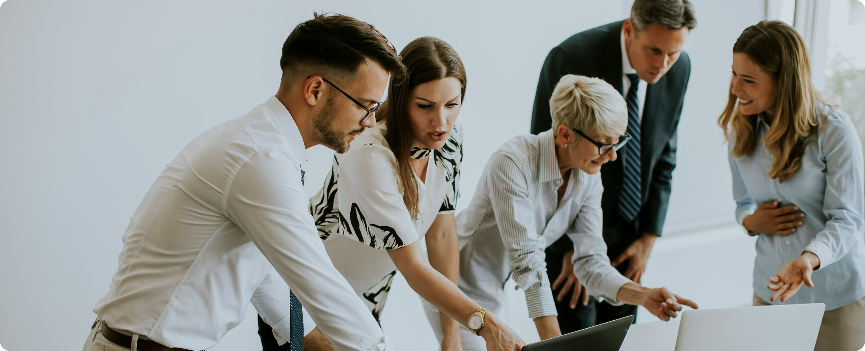 Five professionals gathered around a laptop in an office, discussing work with focused and engaged expressions.