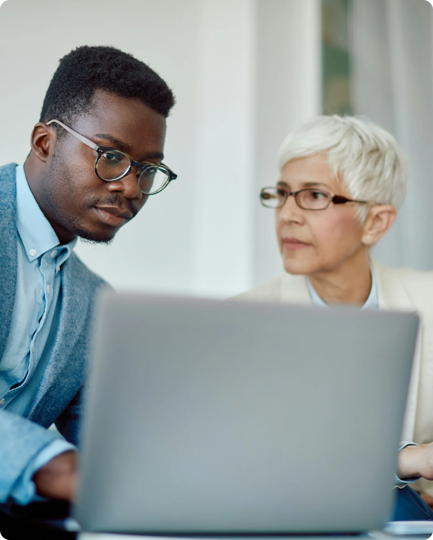Two professionals wearing glasses working together and looking at a laptop screen.
