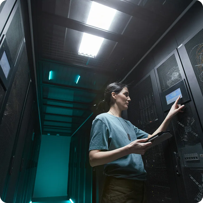 Technician in a server room interacts with a touch screen panel while holding a tablet.