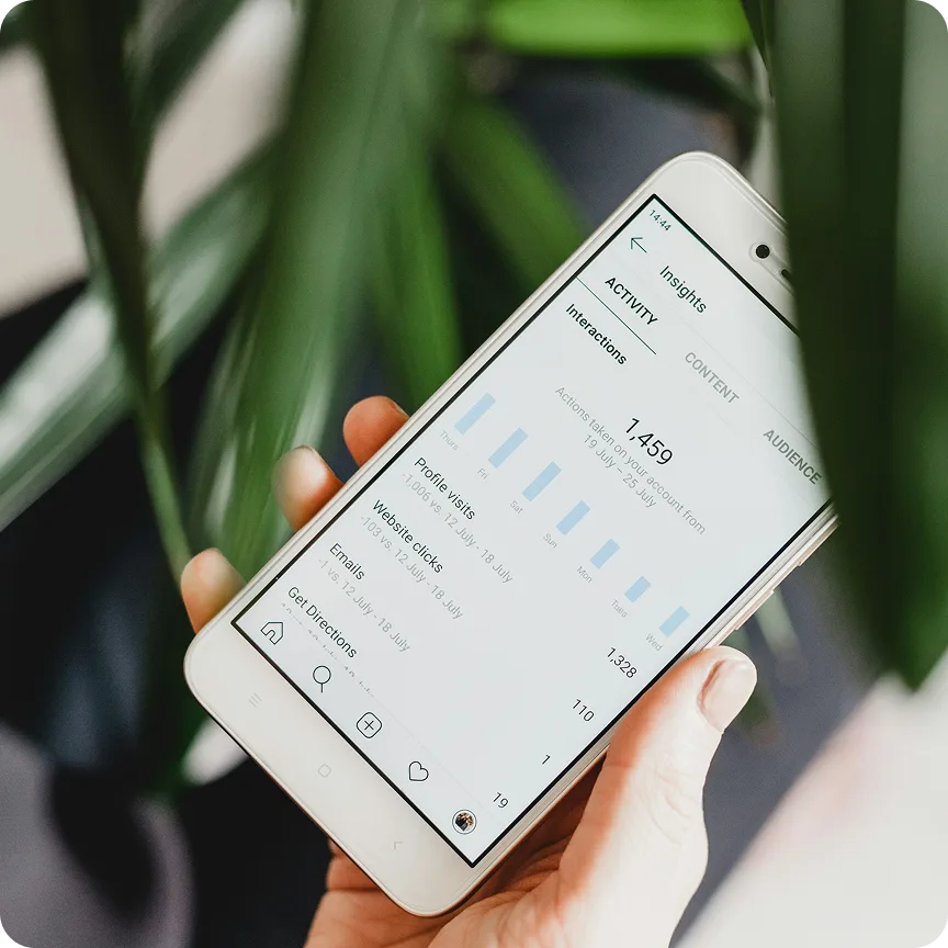 Hand holding a smartphone displaying Instagram Insights activity with interactions data.