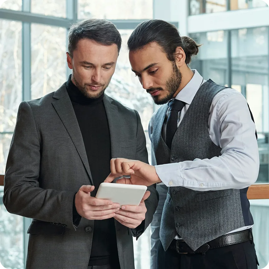 Two businessmen in formal attire looking at and discussing a digital tablet in a modern office.