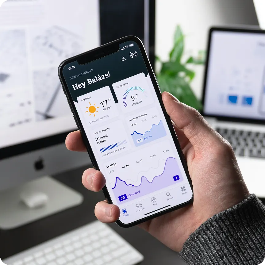 Hand holding smartphone displaying a weather and environment app with temperature, air quality, noise pollution, water quality, and traffic data.