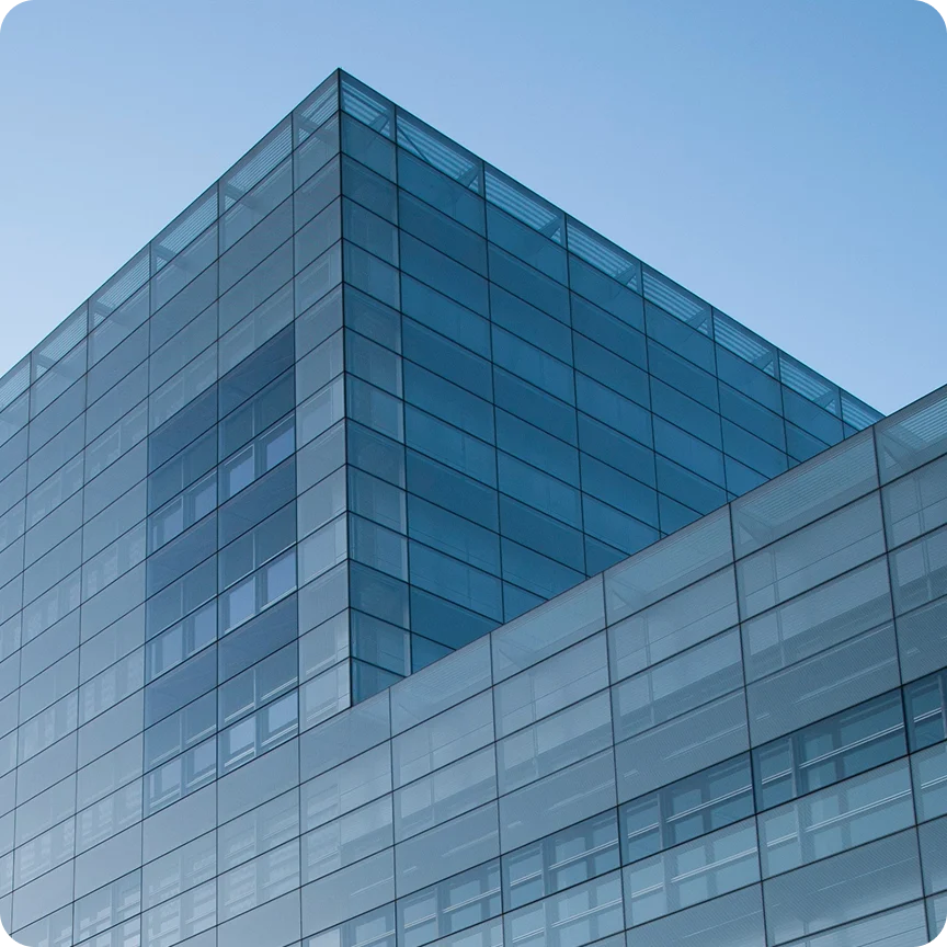 Modern glass office building with reflective blue windows against a clear sky.