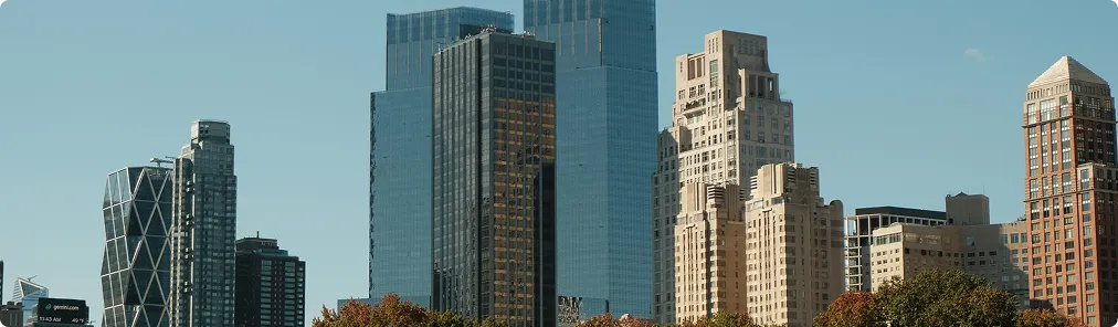 City skyline with a mix of modern glass skyscrapers and older stone buildings under a clear blue sky.
