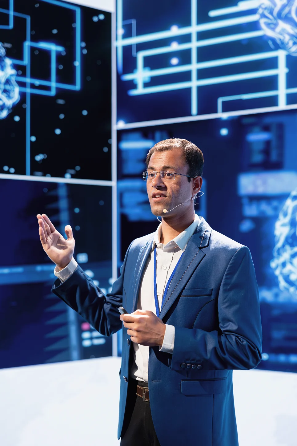 Man in blue suit giving a tech presentation with digital interface graphics in the background.