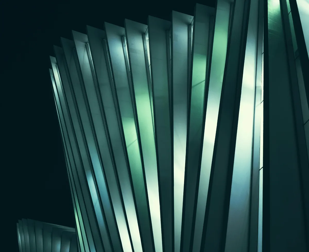 Close-up of illuminated modern glass building panels at night with green and blue reflections.