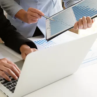 Two people analyzing business charts on tablet and laptop in a work meeting.