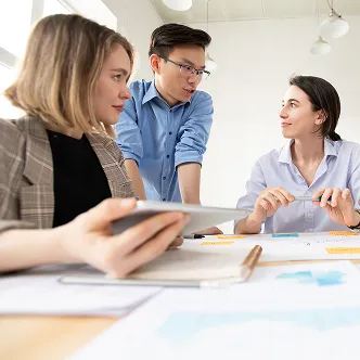 Three colleagues discussing a project around a table with documents and tablets in a modern office.