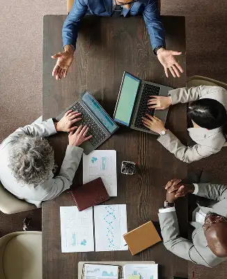 Four business people around a table with laptops and charts, collaborating in a meeting.