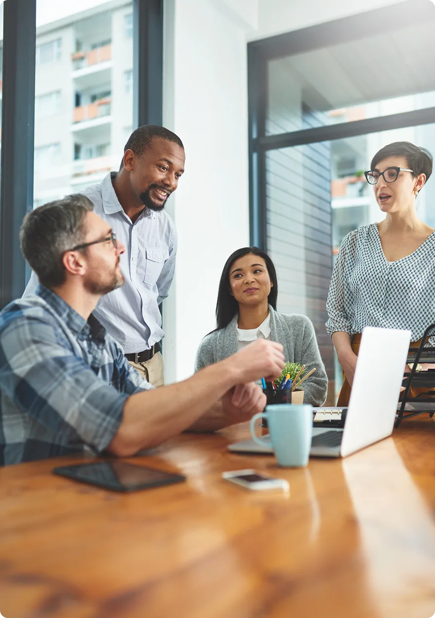 Four diverse colleagues having a casual meeting around a table with a laptop and coffee mug.