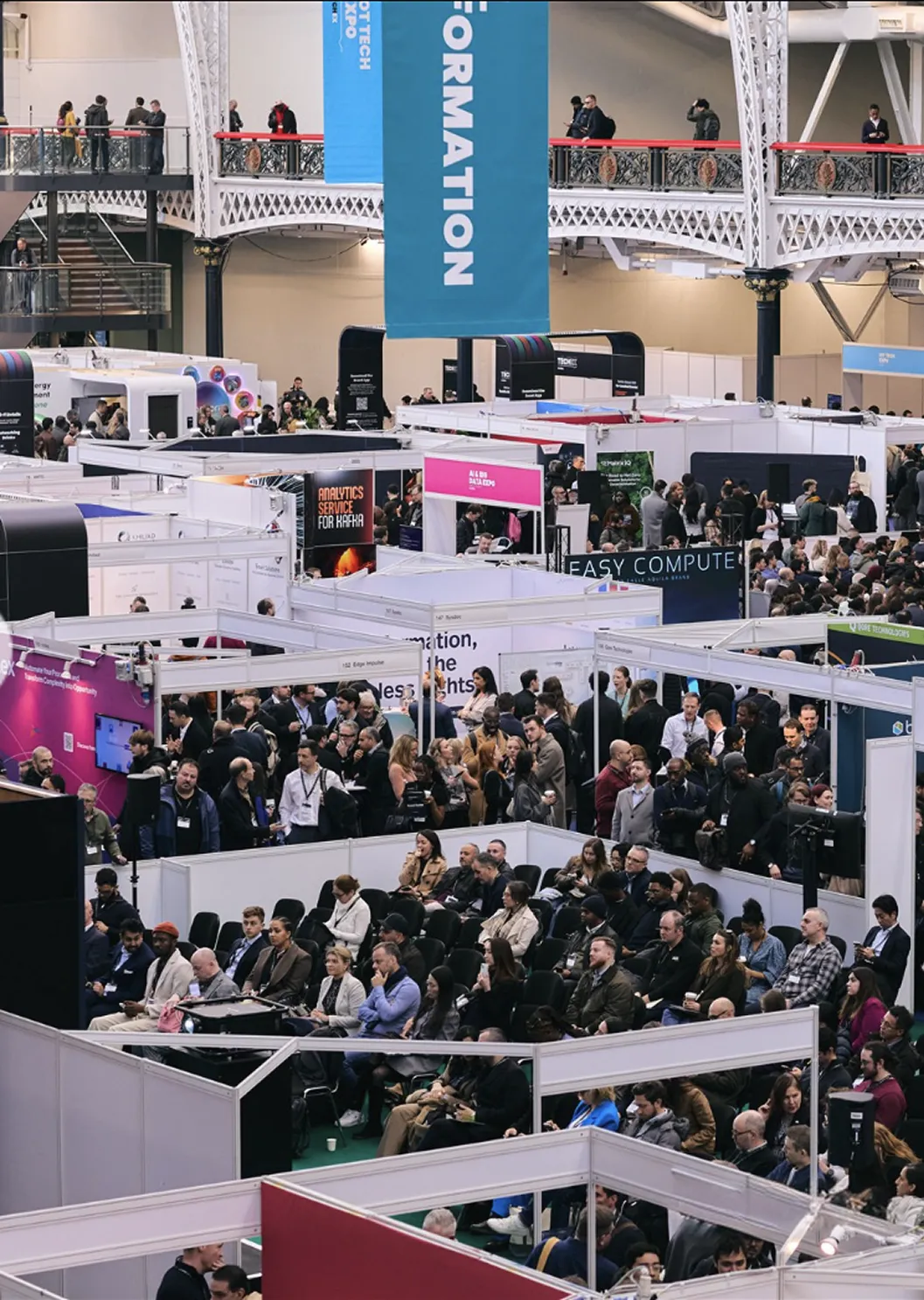 Large crowd attending a busy tech expo with exhibition booths and seated audience in a hall.