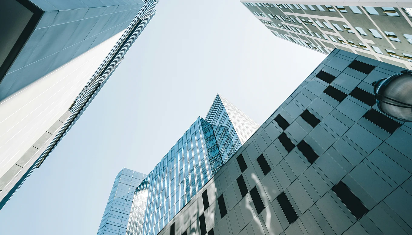 Upward view of modern office buildings with glass and concrete facades under clear sky.