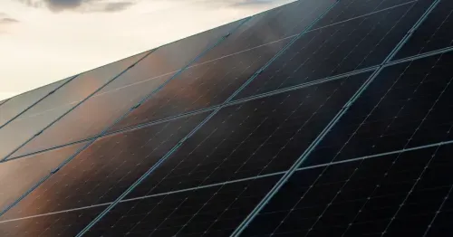 Close-up of solar panels reflecting sky with clouds, capturing clean renewable energy technology.