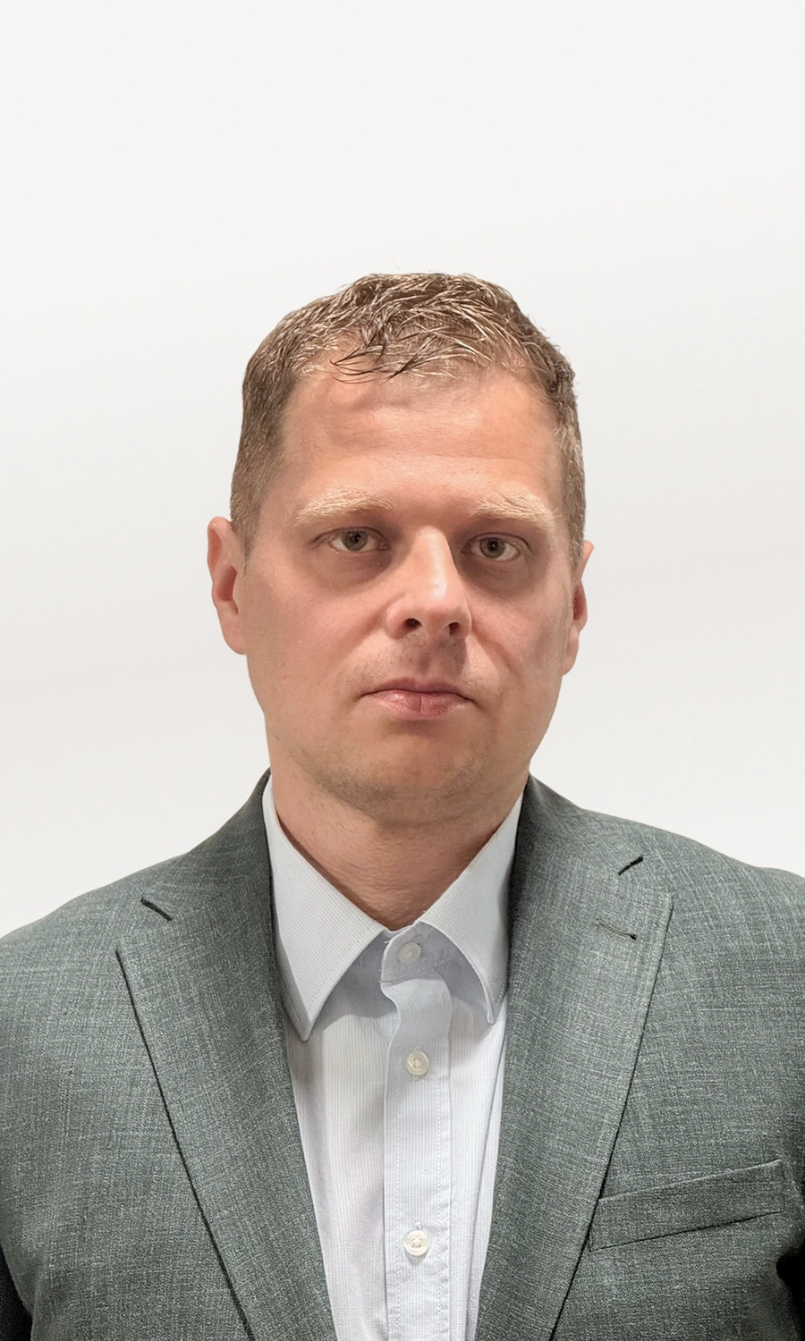 Man with short light brown hair wearing a gray suit jacket and white dress shirt against white background.