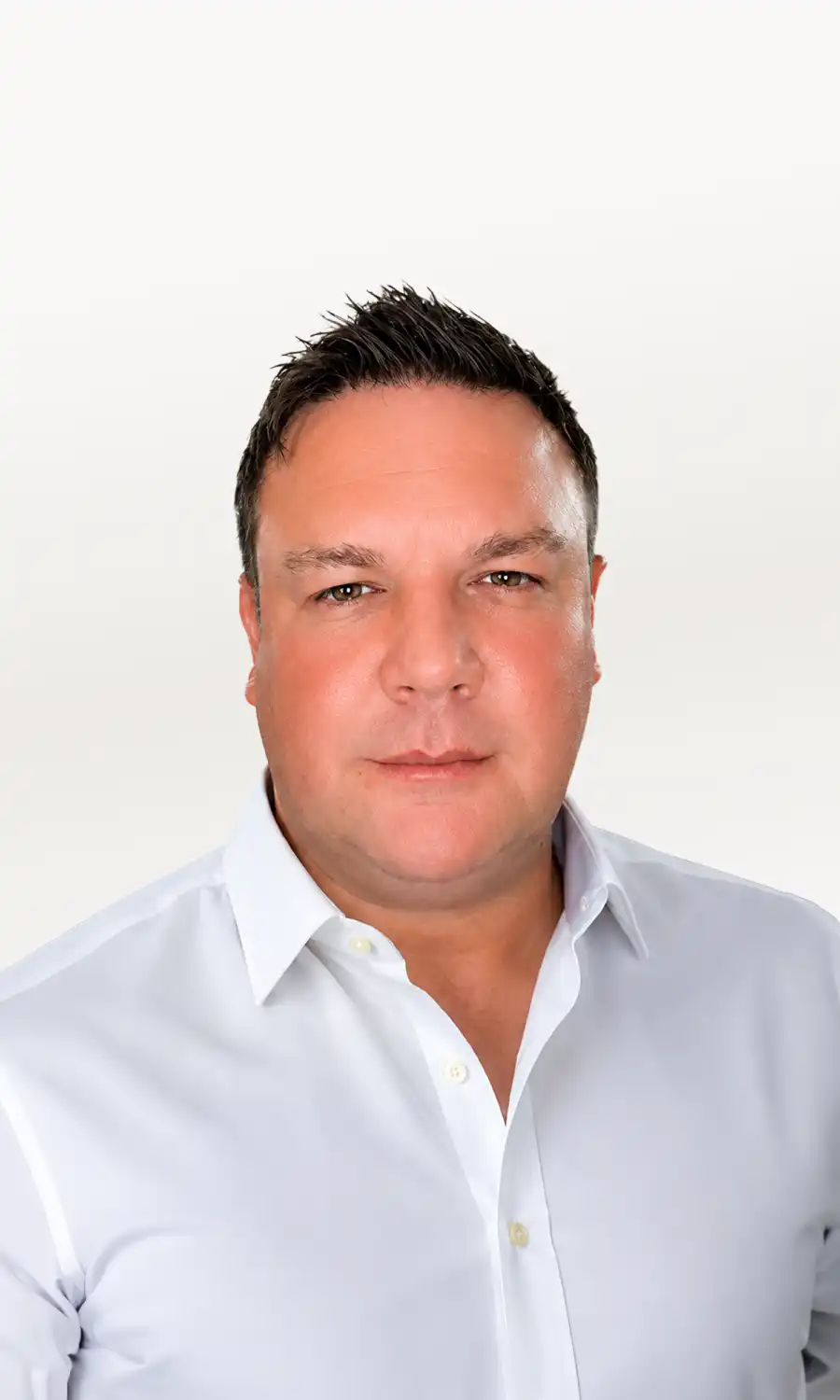 Man with short dark hair wearing a white button-up shirt against a plain light background.