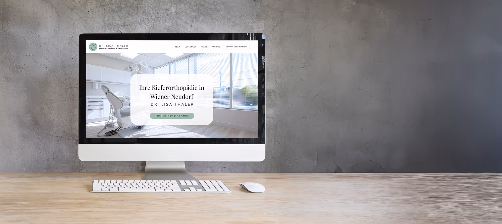 Desktop-Computer auf einem Holzschreibtisch, auf dem die Webseite einer Zahnklinik mit moderner kieferorthopädischer Praxiseinrichtung und Buchungsbutton angezeigt wird.
