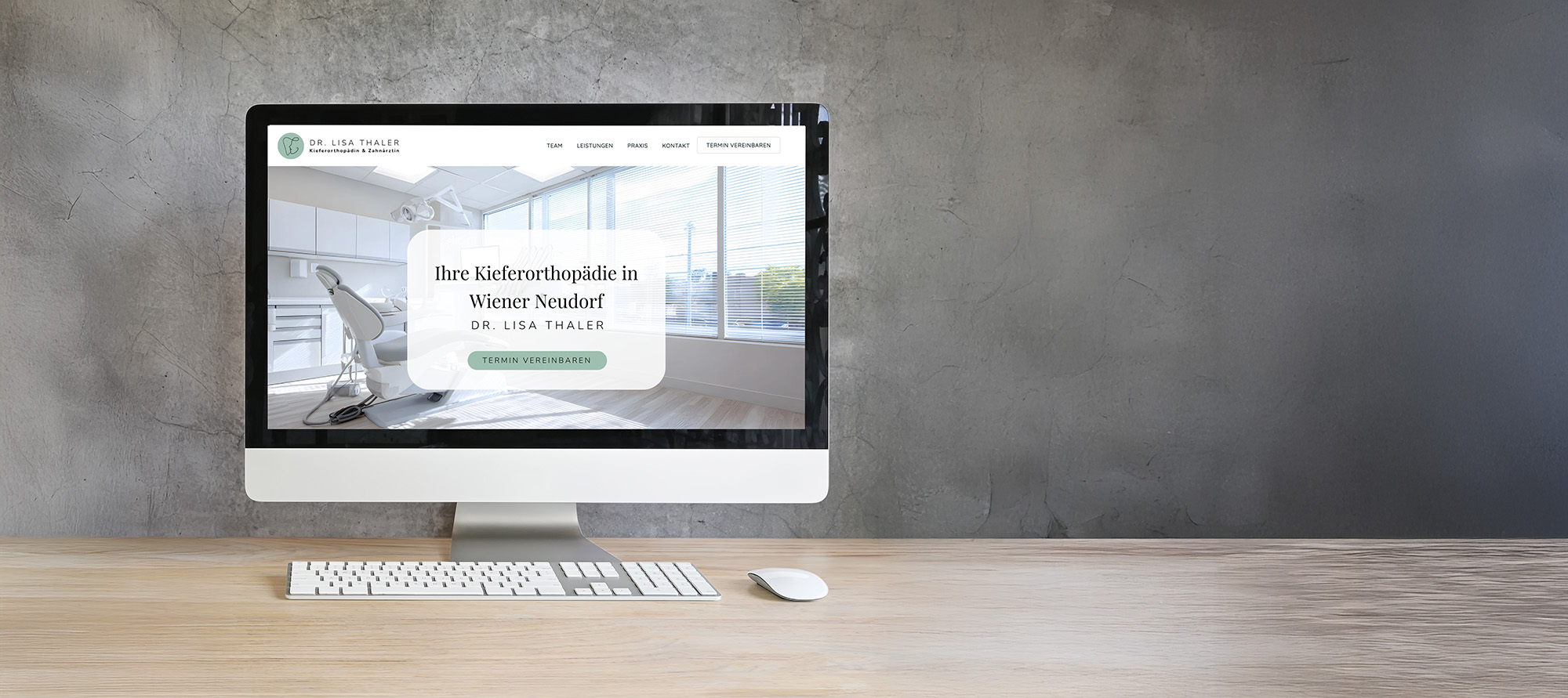 Desktop-Computer auf einem Holzschreibtisch, auf dem die Webseite einer Zahnklinik mit moderner kieferorthopädischer Praxiseinrichtung und Buchungsbutton angezeigt wird.